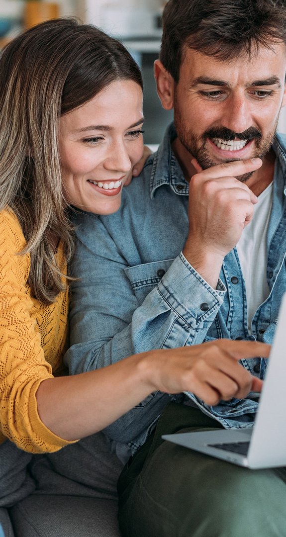 Mann und Frau auf der Couch, beide schauen lachend auf einen Laptop. Symbolisiert schnelles Glasfaser-Internet von ENTEGA in Darmstadt.