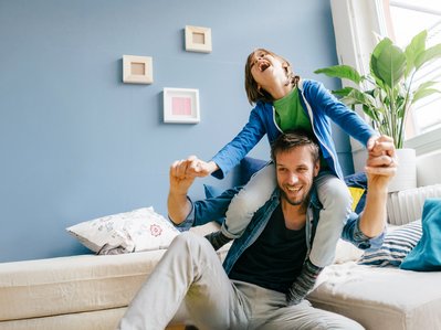 Kind auf den Schultern eines Mannes, beide lächeln. Symbolisiert Wohlfühlatmosphäre mit ENTEGA Kälte- und Klimatechnik.