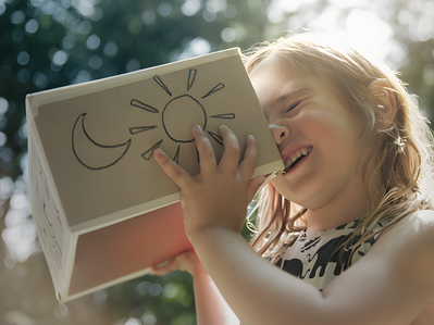Bild zeigt Mädchen, das einen Karton mit Sonne und Mond an ihr Gesicht drückt – Thema: Tag- und Nachtstrom.