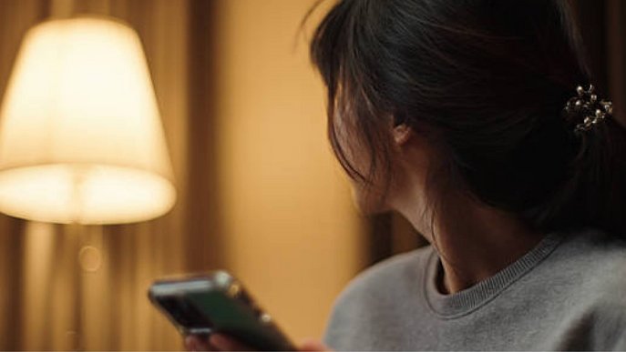 Bild zeigt Frau, die auf eine Lampe blickt und ihr Smartphone hält – Thema: Strom-Ratgeber.